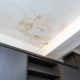 Large brown water stains and moisture damage spreading across a white ceiling above dark wooden cabinets.