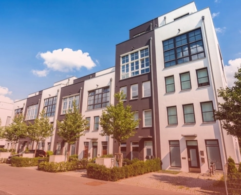 A row of modern multi-story apartment buildings with white and dark gray facades on a bright sunny day.