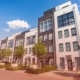 A row of modern multi-story apartment buildings with white and dark gray facades on a bright sunny day.