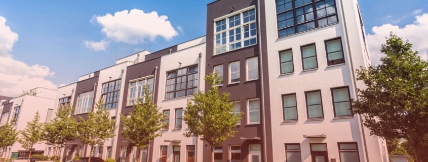 A row of modern multi-story apartment buildings with white and dark gray facades on a bright sunny day.