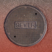 When Is the City Responsible for Sewer Lines Overhead view of a round metal manhole cover stamped with the word "SEWER" set in asphalt pavement.