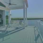 deck inspections Elevated covered patio deck with lounge chairs and white railings overlooking a scenic waterfront view.