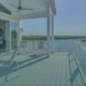 Elevated covered patio deck with lounge chairs and white railings overlooking a scenic waterfront view.