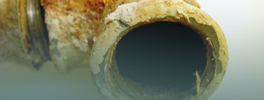 Close-up cross-section of a deteriorated Orangeburg sewer pipe showing delaminating, brittle layers and heavy rust and mineral buildup around the opening.